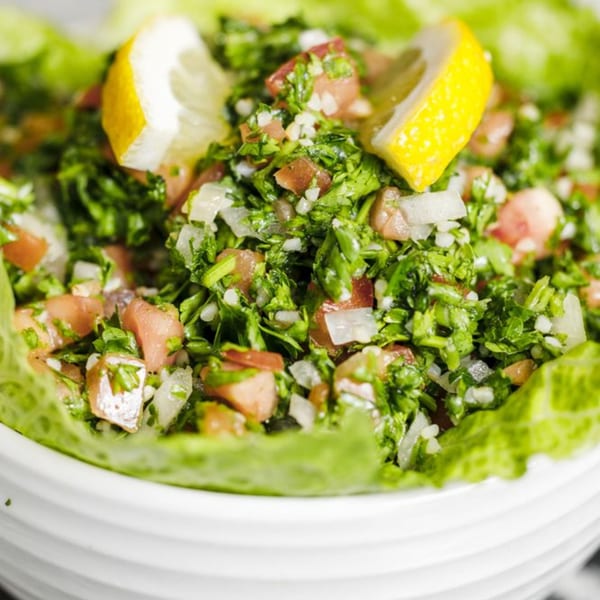 Close-up of a vibrant green tabbouleh salad with diced tomatoes, onions, and lemon wedges.