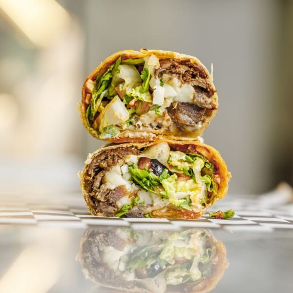 Two halves of a Shawarma Shack wrap, revealing beef, lettuce, and white sauce, stacked on a reflective surface.