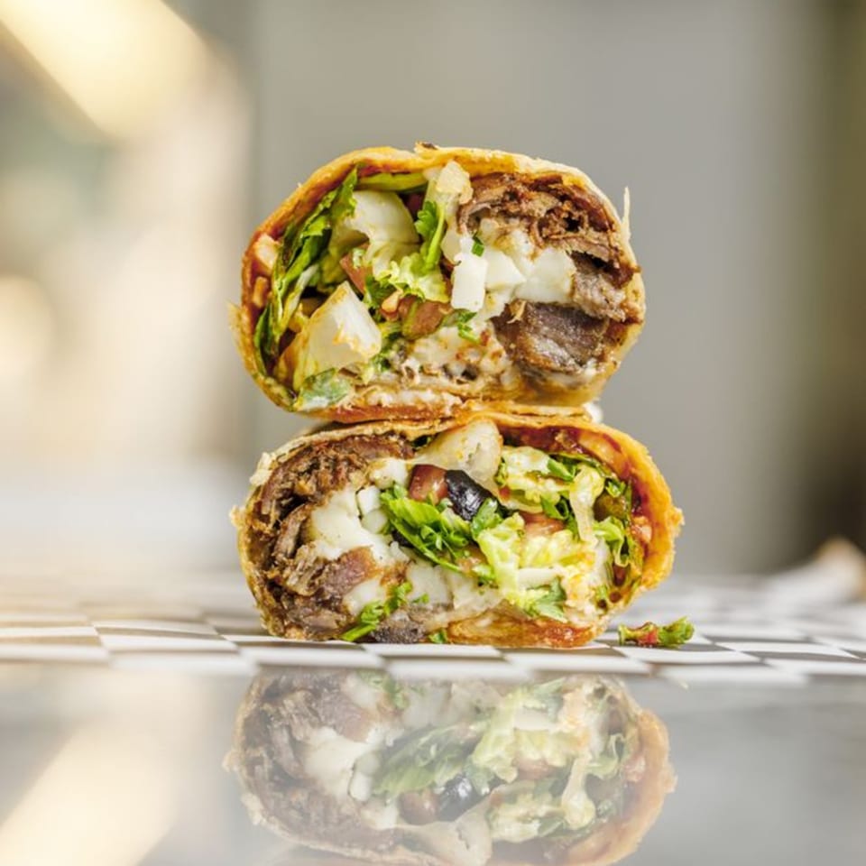 Two halves of a Shawarma Shack wrap, revealing beef, lettuce, and white sauce, stacked on a reflective surface.
