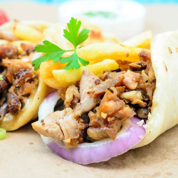 Two chicken gyros with fries, red onion, and parsley, with a white sauce in the background.