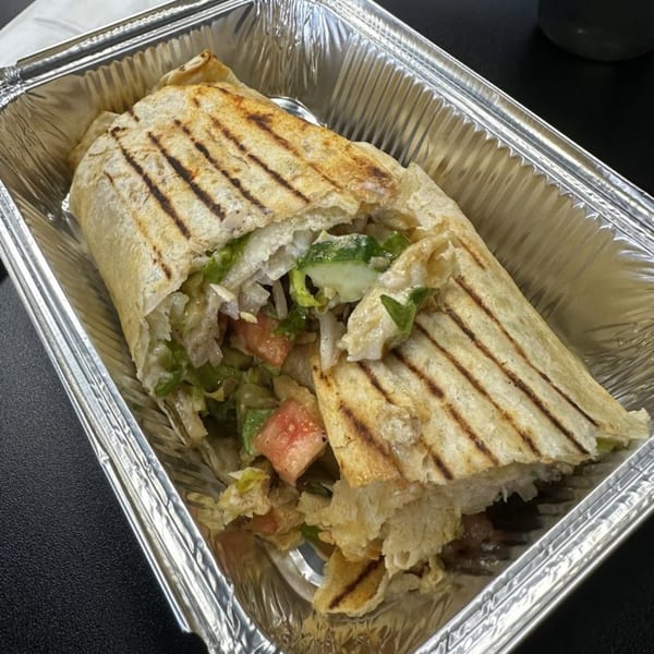 Grilled wrap with lettuce, tomatoes, and meat, served in a silver foil container.