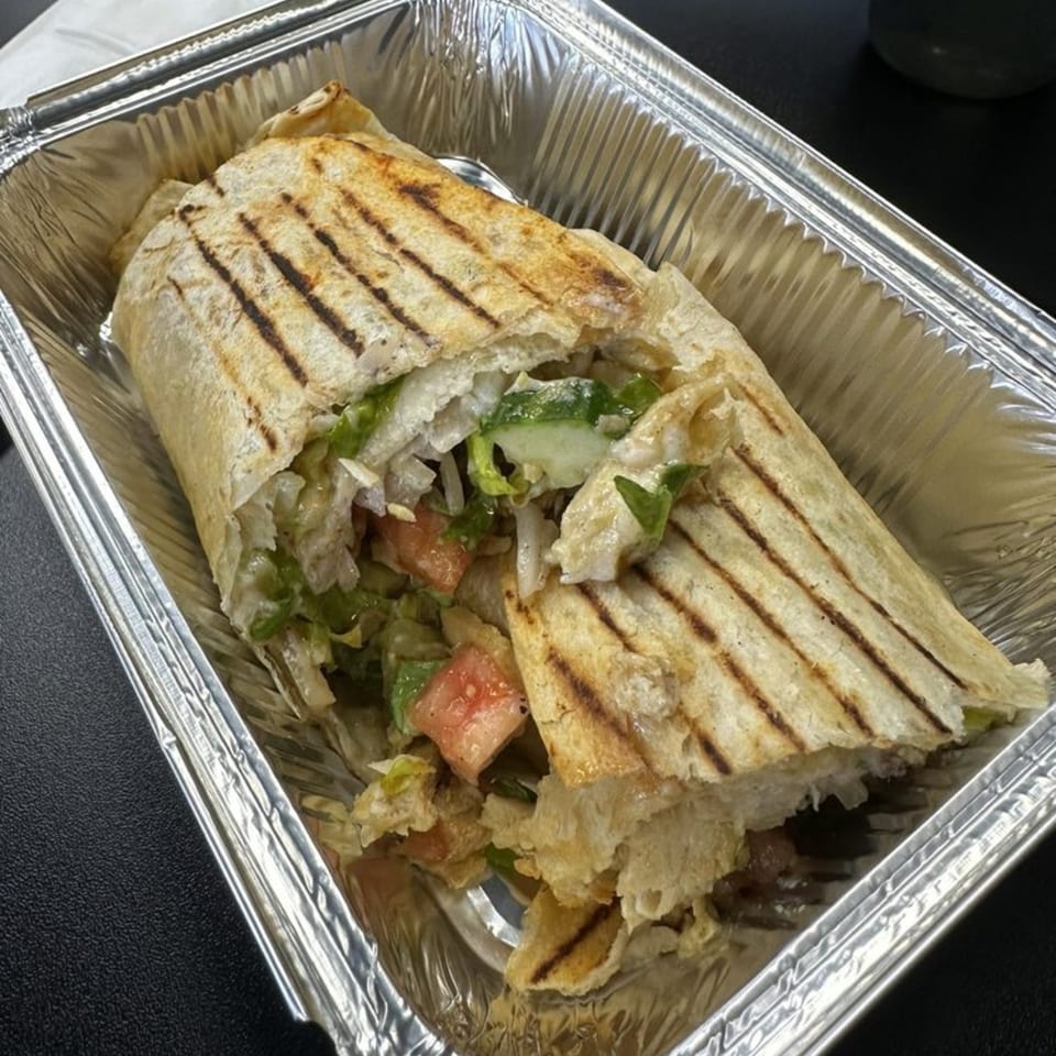 Grilled wrap with lettuce, tomatoes, and meat, served in a silver foil container.