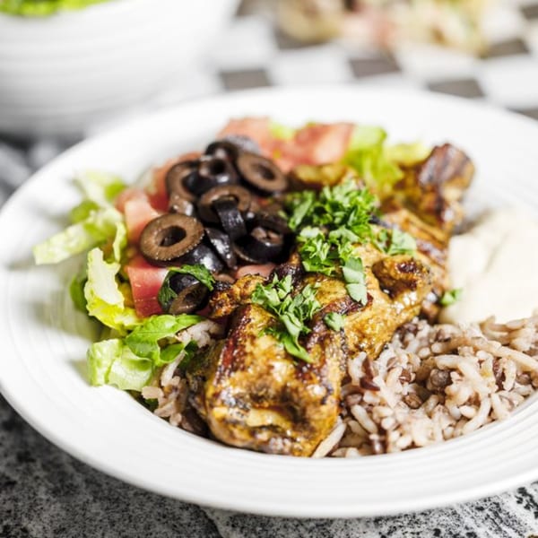 Grilled chicken with rice, salad, black olives, and parsley on a white plate.