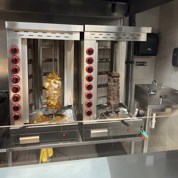 Two vertical rotisseries with chicken and beef shawarma cooking in a commercial kitchen.