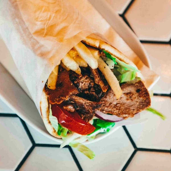 A delicious gyro with meat, french fries, lettuce, tomatoes, and onions wrapped in pita bread.