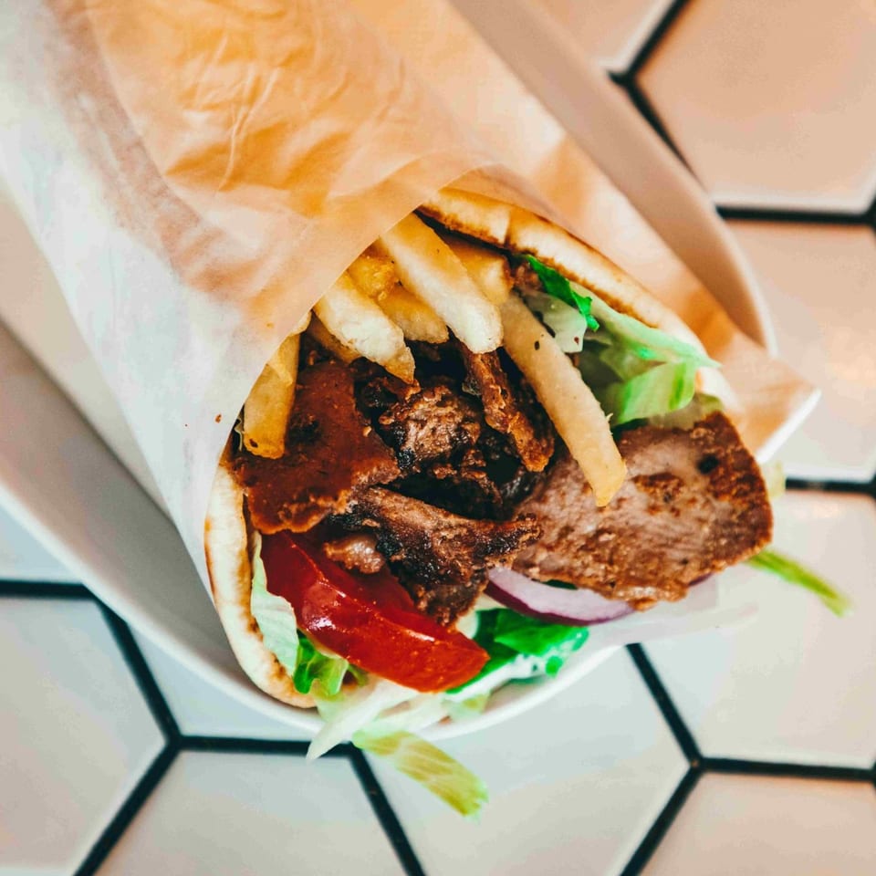 A delicious gyro with meat, french fries, lettuce, tomatoes, and onions wrapped in pita bread.