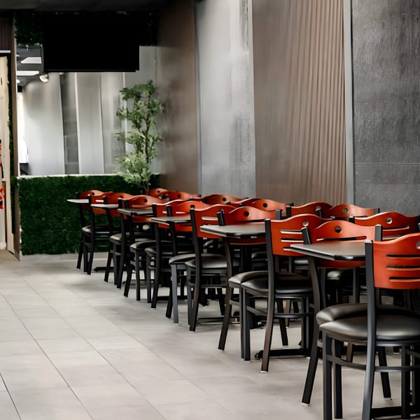 Empty dining area at Shawarma Shack with rows of black tables and red-backed chairs.
