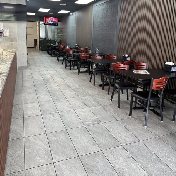 Empty dining room at Shawarma Shack with black tables, red chairs, and a TV playing in the background.